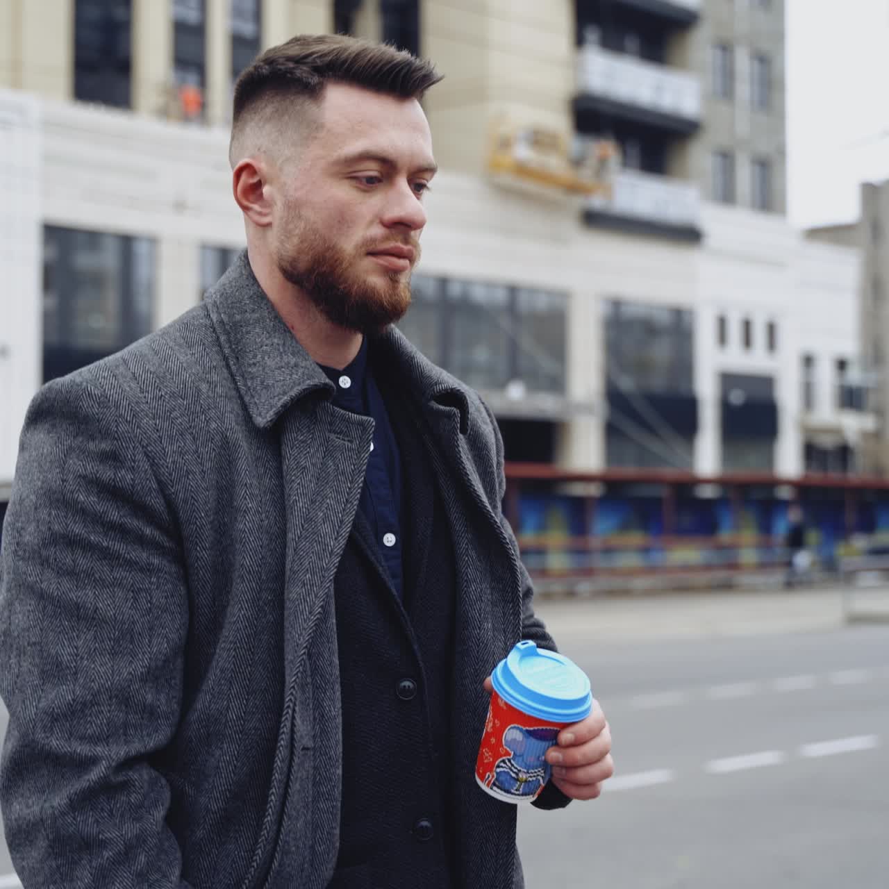 Charming young businessman dressed in suit and coat drinking coffee. Man outside a modern building