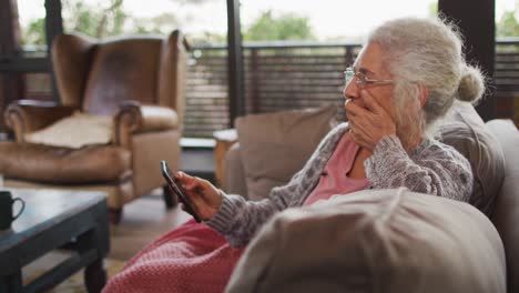 Senior-mixed-race-woman-sitting-on-sofa-using-smartphone