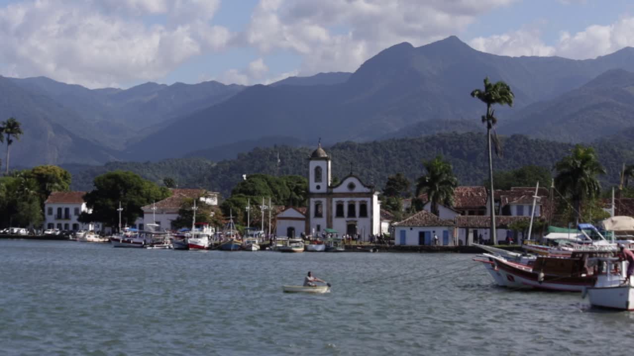 Man rowing boat in Paraty harbor with historic Igreja Santa Rita in the background, Brazil