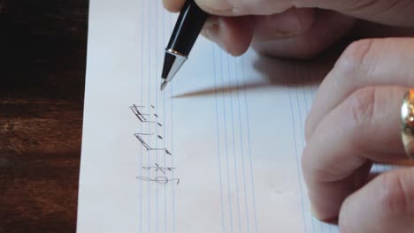 composer writing music notes on sheet with pen hand close up