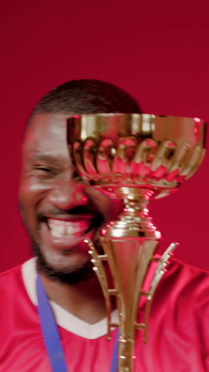 Video verticale: Uomo sorridente in maglia rossa con medaglia che agita una coppa d'oro dopo una vittoria in studio, spazio per il testo.