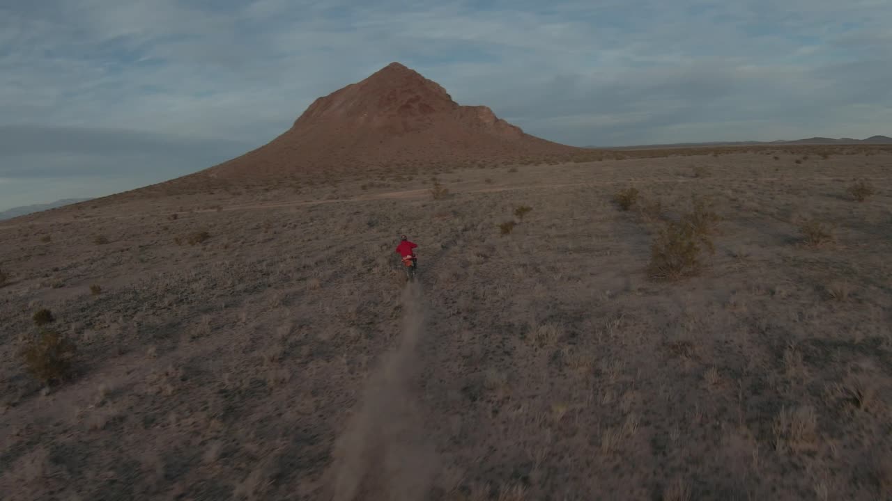 un motociclista acelera a través del terreno accidentado del desierto de mojave al atardecer - vista aérea de seguimiento