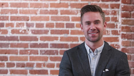 Young-Businessman-Standing-Against-Brick-Wall-In-Modern-Office