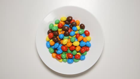 vista de arriba: dulces de colores aparecen en un plato blanco en una mesa blanca (movimiento de parada)