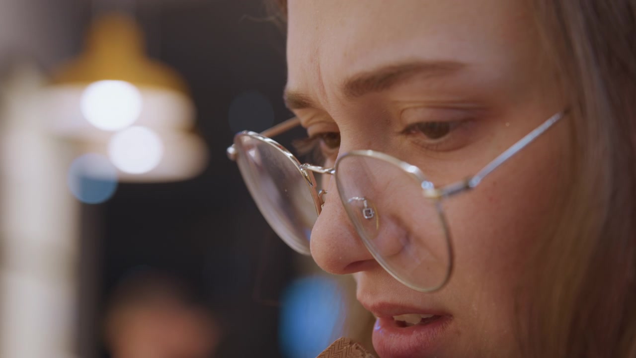 Primo piano di donna angosciata con lacrime riflettenti ed effetti di luce di sfondo. Immagine femminile espressiva che raffigura vulnerabilità e intensità emotiva in mezzo all'ambiente sfocato di un caffè.