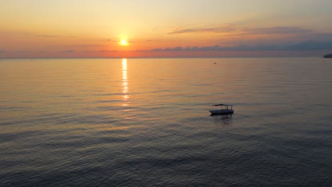 aerial view of a single fishing boat on calm morning waters with warm sunrise glow