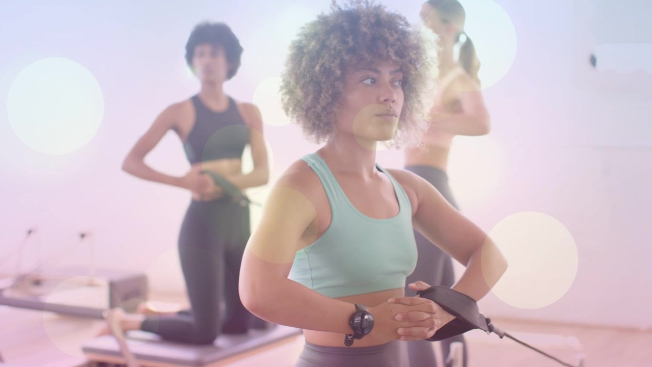 Lead woman clasping Pilates reformer strap, engaging core for posture, shifting gaze with bokeh