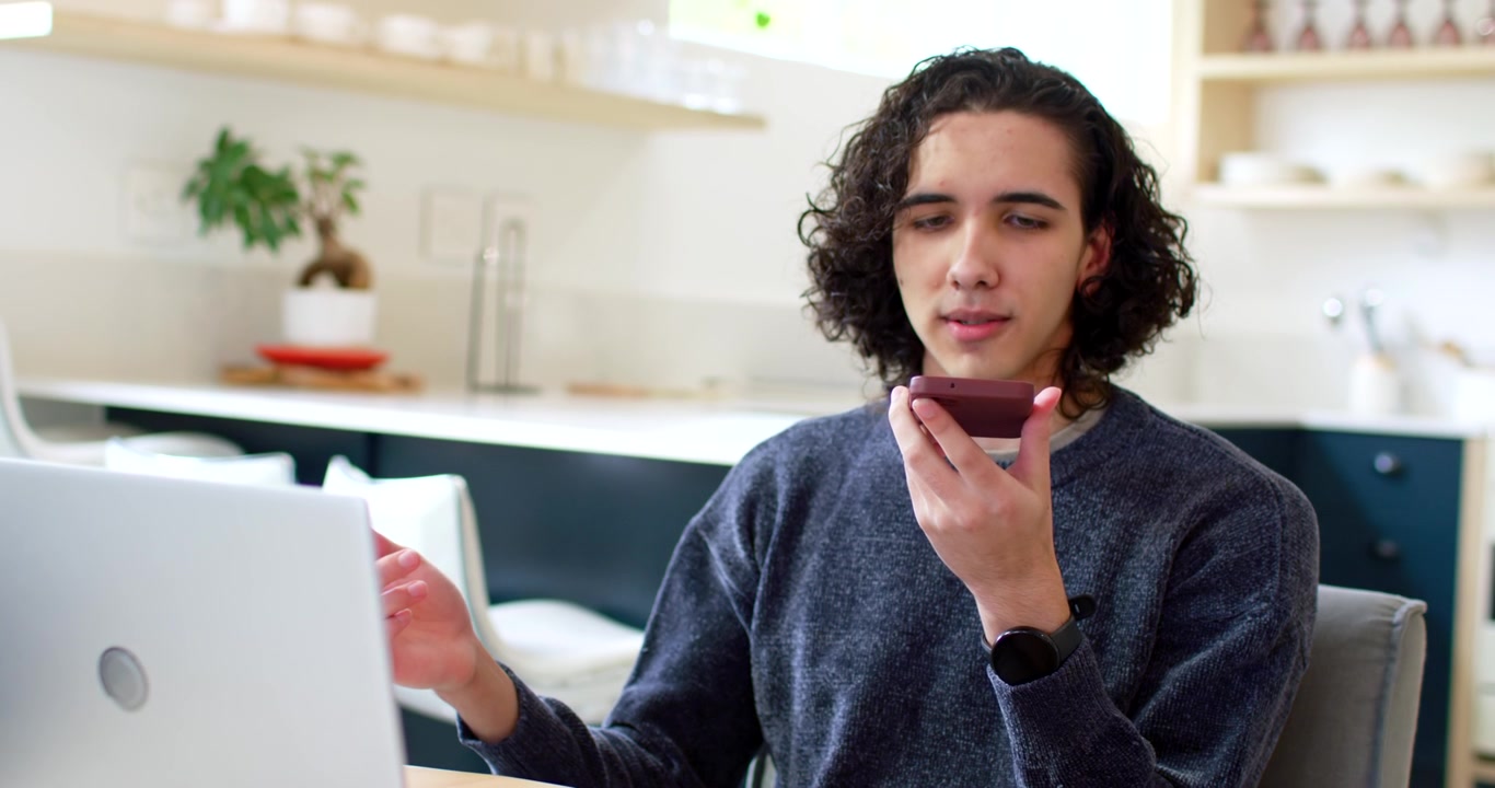 Uomo afroamericano in cucina che registra per lavoro, parla al telefono, con laptop e microfono in evidenza.