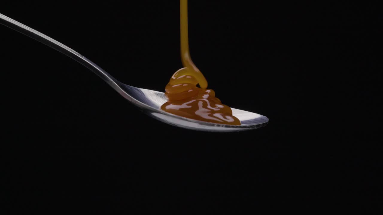 Static shot of a spoon being poured over caramel against black background