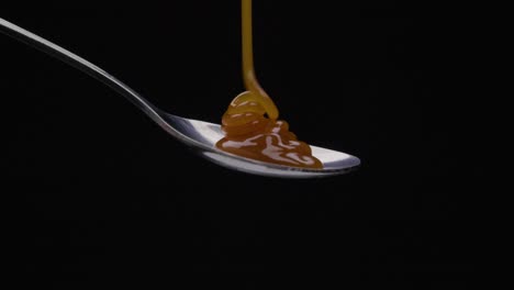 static shot of a spoon being poured over caramel against black background