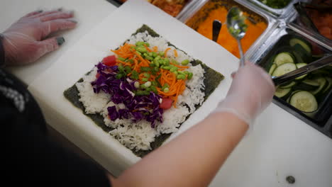 overhead shot of worker sprinkling green onions onto poke burrito, worker assembles pokerrito, slow motion 4k