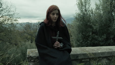 religious woman prays with crucifix in the cemetery among the trees