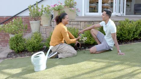 Feliz-Pareja-Gay-Diversa-Haciendo-Jardinería-Y-Hablando-Arrodillado-En-Un-Jardín-Soleado,-Cámara-Lenta