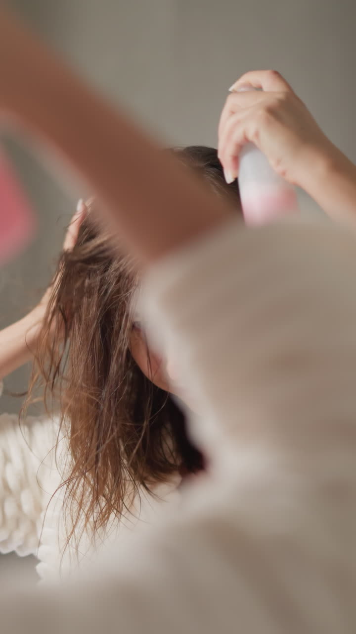 잘 관리 된 여성은 밝은 화장실에서 머리카락에 스프레이를 뿌립니다. 젊은 여성은 머리카락 관리 치료를 스프레이 수분 혈청을 느린 동작으로합니다.