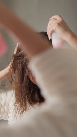 una mujer bien cuidada salpica spray en el cabello en un baño iluminado. una mujer joven hace tratamientos para el cuidado del cabello rociando suero hidratante en cámara lenta