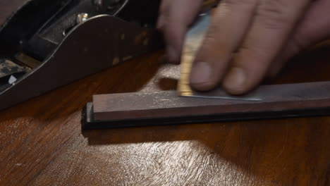 La-Mano-Derecha-Masculina-Afila-La-Hoja-De-Avión-De-Madera-Antigua-Sobre-Piedra-De-Afilar