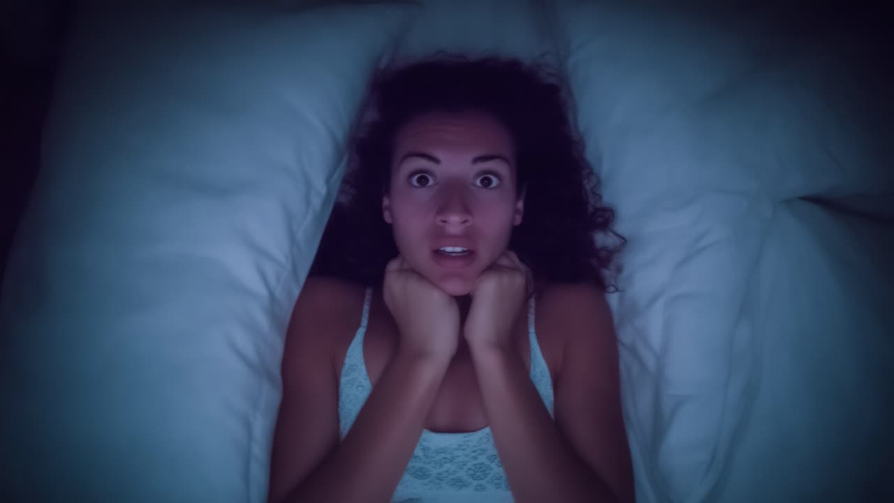 Anxiety and Fear: A Woman's Expression of Distress While Awake at Night, Captured in a Dark Room Surrounded by Pillows and Sheets