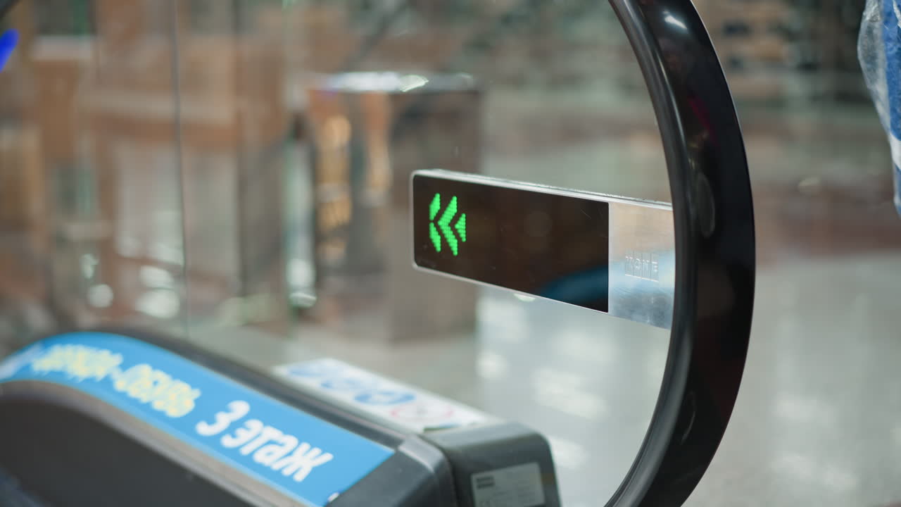 close up of downwards green arrow display mounted at moving walkway entrance in shopping mall corridor with silhouettes of passing pedestrians reflected on glass and steel surfaces