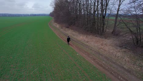 Fotógrafo-Masculino-Solo-Con-Abrigo,-Sombrero-Y-Mochila-Viaja-A-Lo-Largo-De-Un-Camino-Rural-En-La-Naturaleza-A-Principios-De-La-Primavera