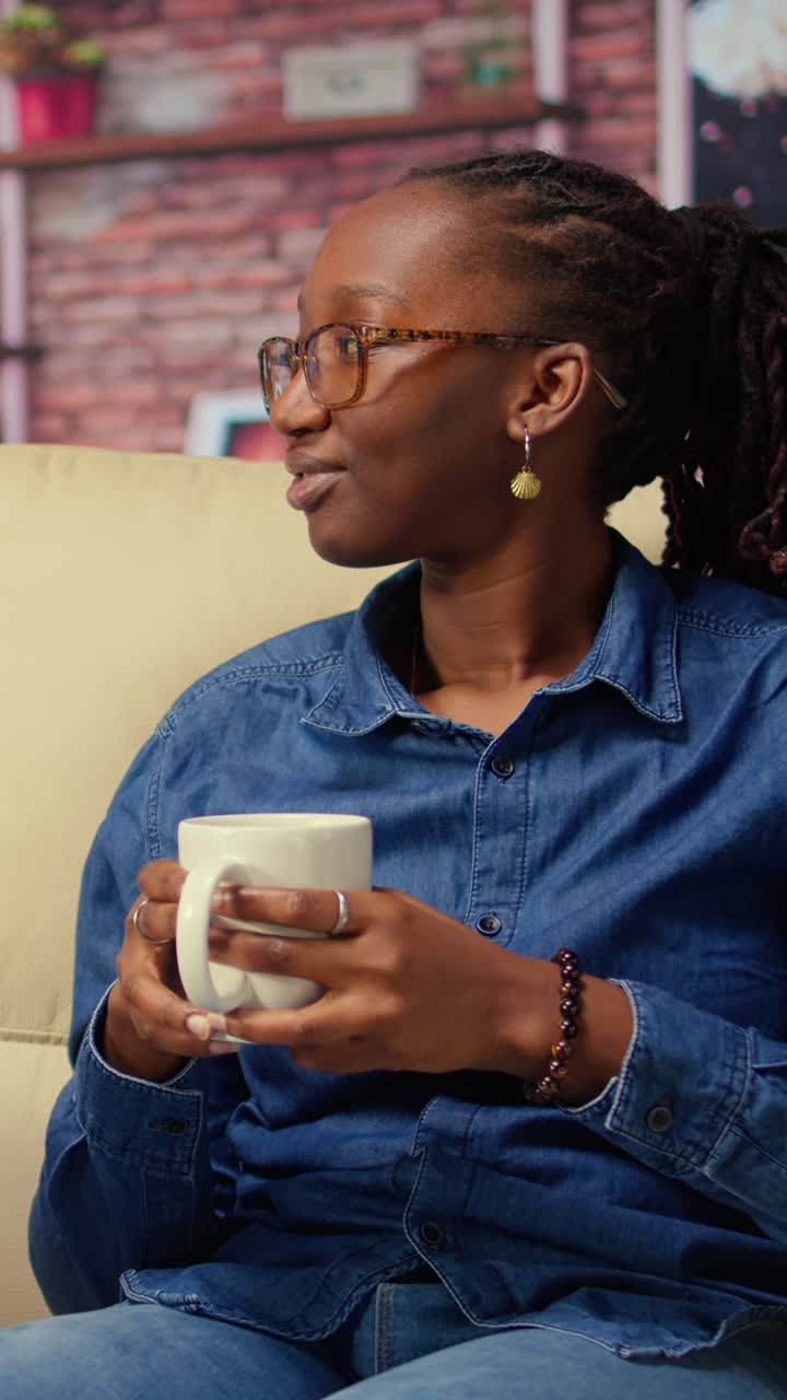 Afroamerikansk kvinde taler og smiler i sofaen med et krus