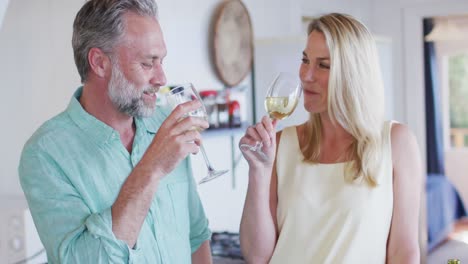 feliz pareja caucásica madura cocinando juntos y bebiendo vino en la cocina