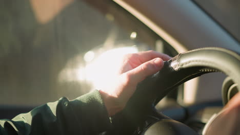 a close-up shot of a man's hand gripping and tapping on a car steering wheel, with sunlight filtering through the window, highlighting the driver's focus and anticipation