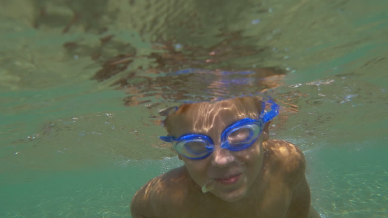 보호 안경 을 입은 소년 이 바물  에서 수영 하고 있다