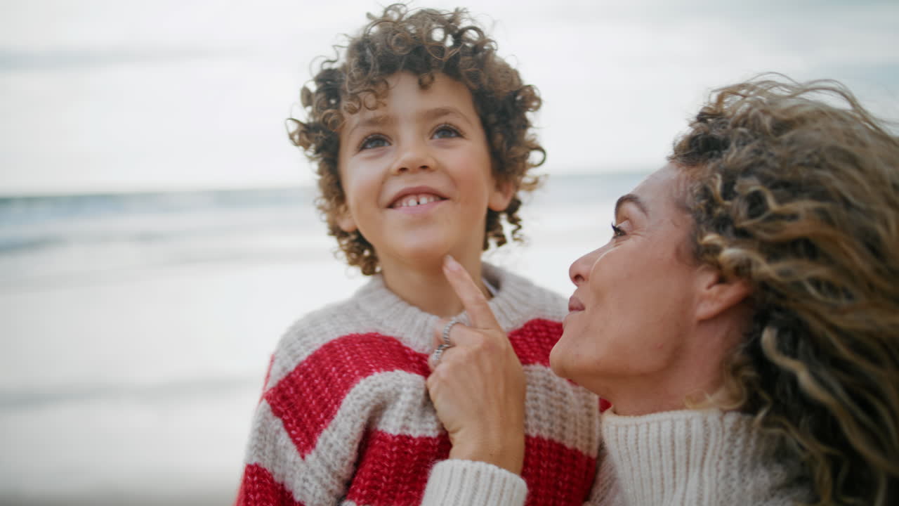 Ritratto di madre e figlio che riposano insieme sulla riva dell'oceano in autunno. Abbraccio familiare allegro.