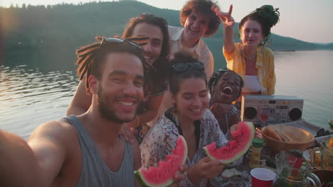 happy friends posing for camera and taking selfie at lake party