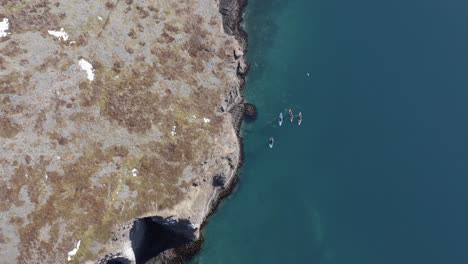 Cuatro-Kayakistas-Moviéndose-A-Lo-Largo-De-La-Costa-Escarpada-Salvaje-De-La-Península-De-Holmanes-De-Islandia,-Antena