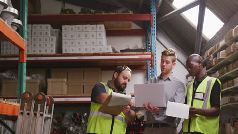 Two-Caucasian-and-an-African-American-male-factory-worker-at-a-factory-pointing,-holding-a-clipboard