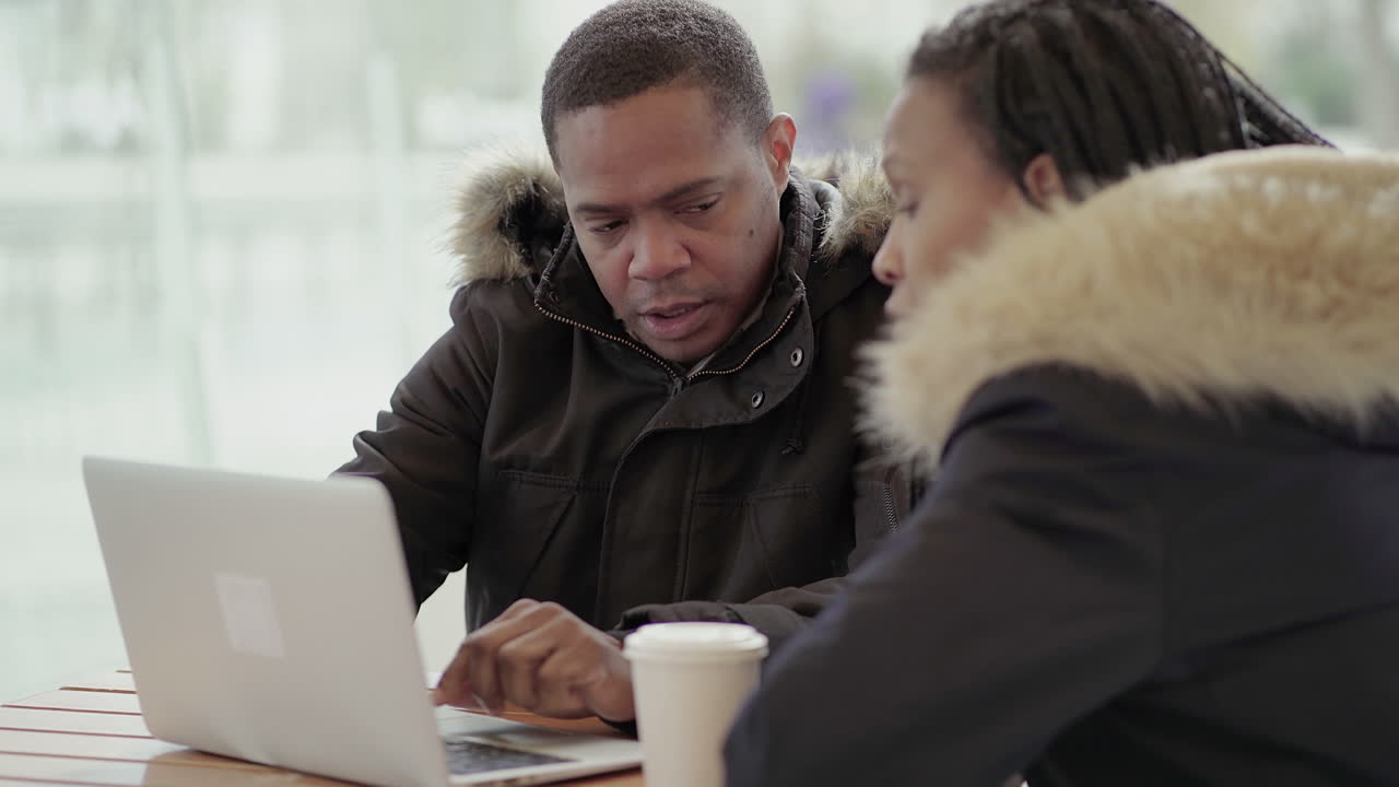 Afro-American middle-aged man in black jacket with fur hood discussing data with Afro-American young girl with braids