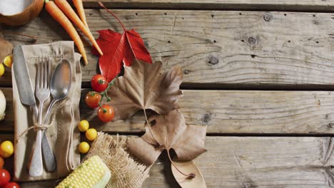 multiple food ingredients, autumn leaves and cutlery with copy space on wooden surface