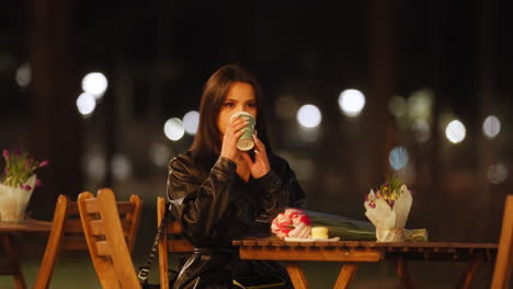 Attractive-young-caucasian-woman-sitting-on-a-terrace-drinking-in-slow-motion-at-night