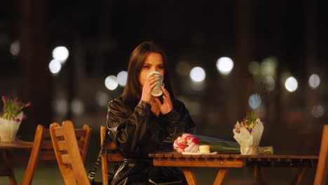 attractive young caucasian woman sitting on a terrace drinking in slow motion at night