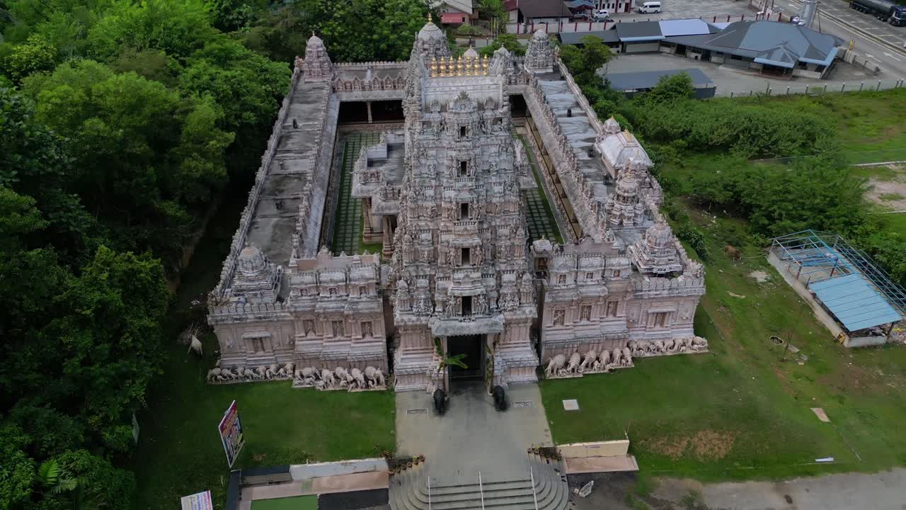 Esterno di un tempio indù ornato con un gopuram imponente, intagli intricati e statue, circondato da un paesaggio verde. Ottimo filmato aereo circolare con drone