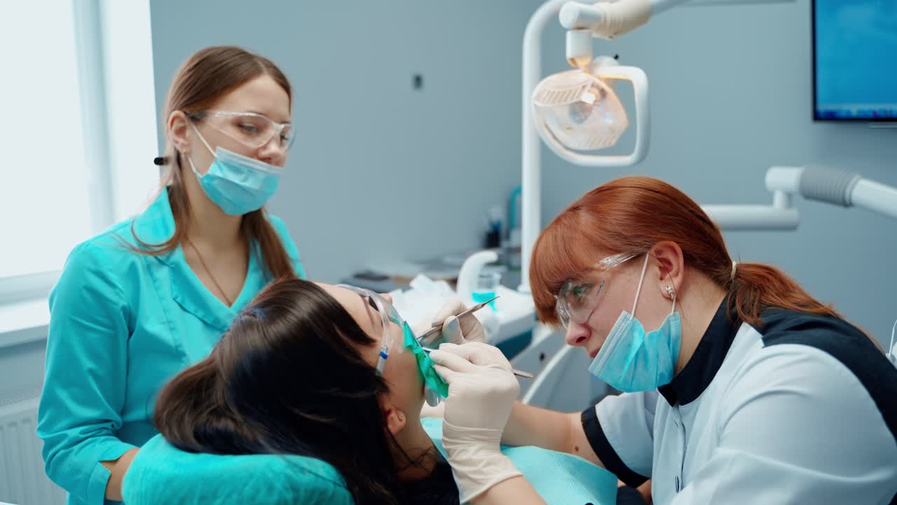 Stomatologist treats tooth with medical tools. Female dentist together with a nurse treating woman's teeth in clinic. Stomatology concept.
