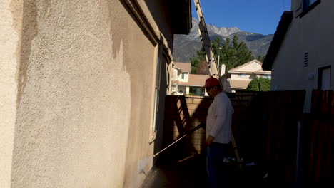 A-cleaning-service-or-painter-tradesman-pressure-washing-a-concrete-wall,-starting-from-the-bottom-and-working-his-way-up