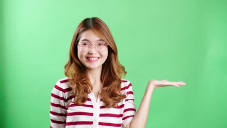 Young-woman-in-studio-pointing-to-object-to-be-graphically-entered-using-chroma-key