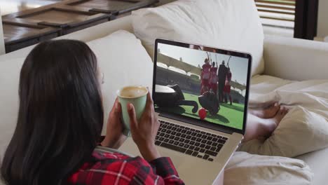 compuesto de una mujer sentada en casa sosteniendo un café viendo un partido de hockey en una computadora portátil