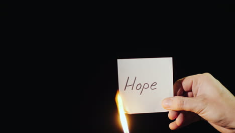 hand holds burning paper with inscription hope