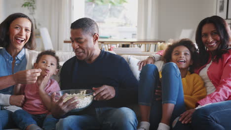three generation african american family sitting on the sofa watching tv and eating popcorn, panning shot