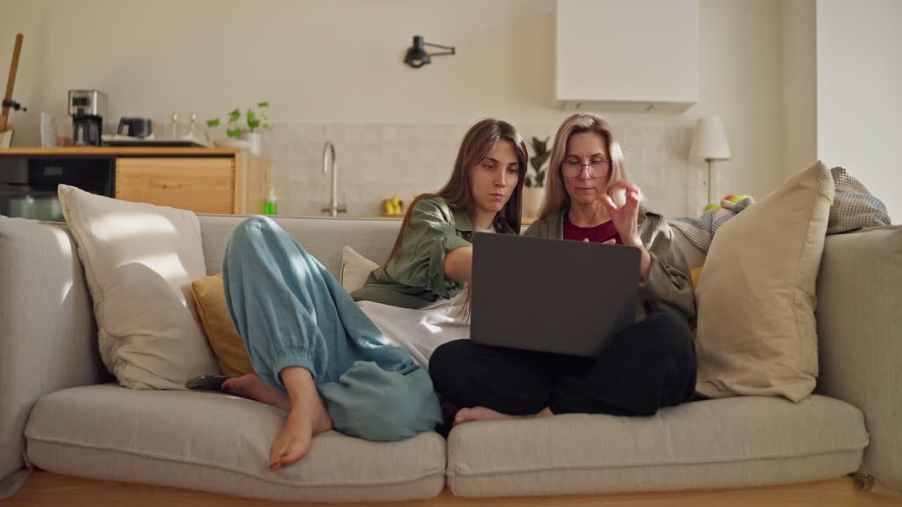madre e hija usando la computadora portátil juntos en el sofá