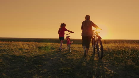 back view: an elderly lady walks with her granddaughter bicycles at sunset 1