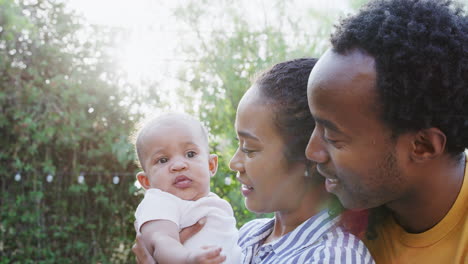 Loving-Parents-Holding-Baby-Daughter-At-Home-Outdoors-In-Garden