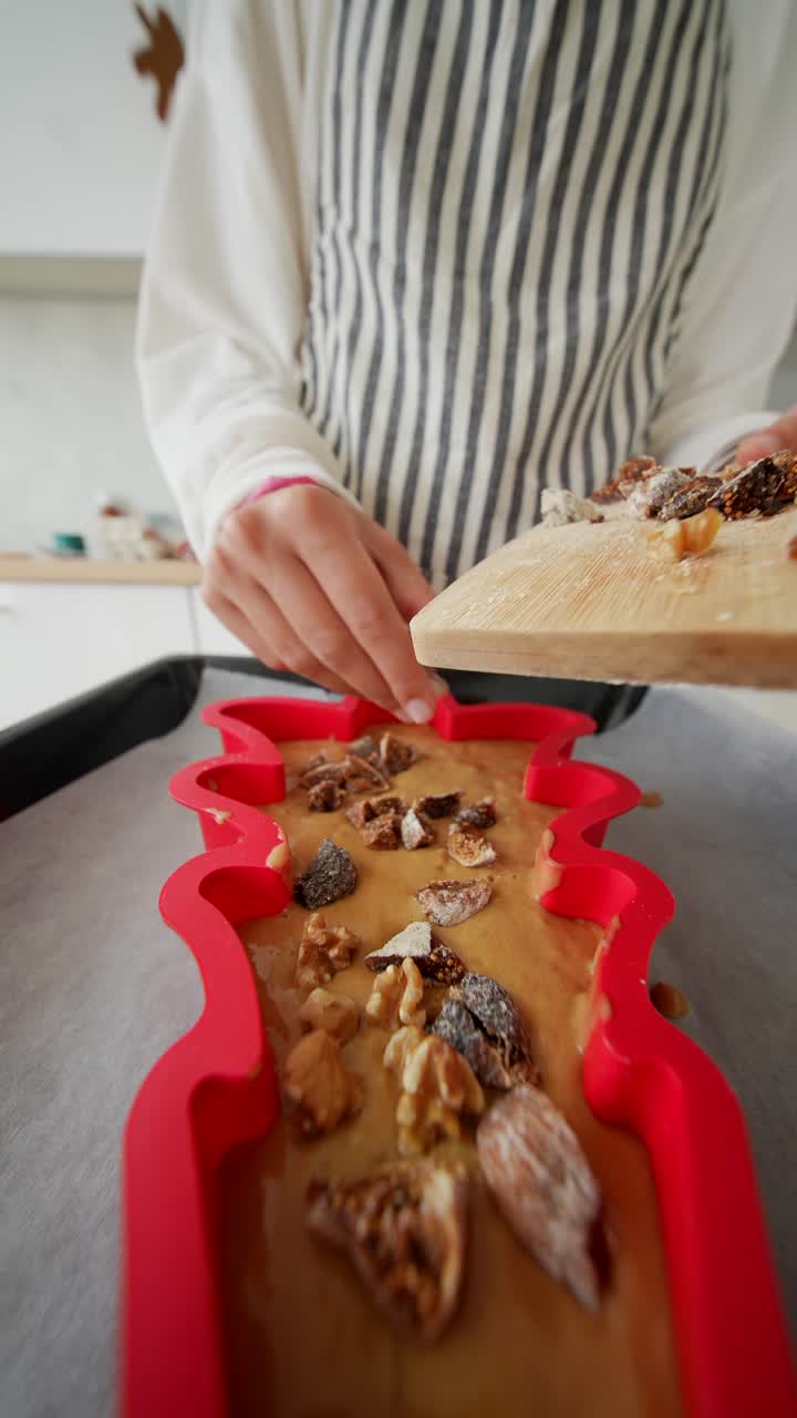 Hands Adding Walnuts and Dried Figs to Cake Batter in Red Mold