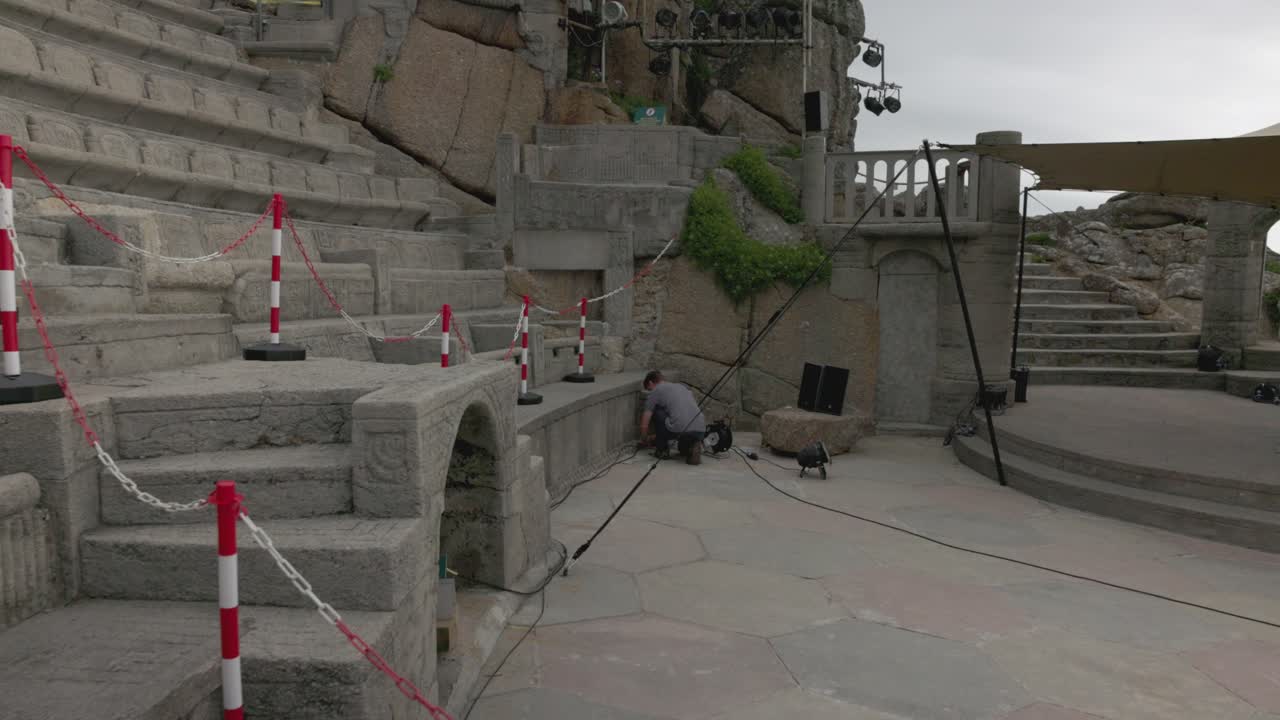 Man setting up stage equipment at an outdoor stone amphitheater
