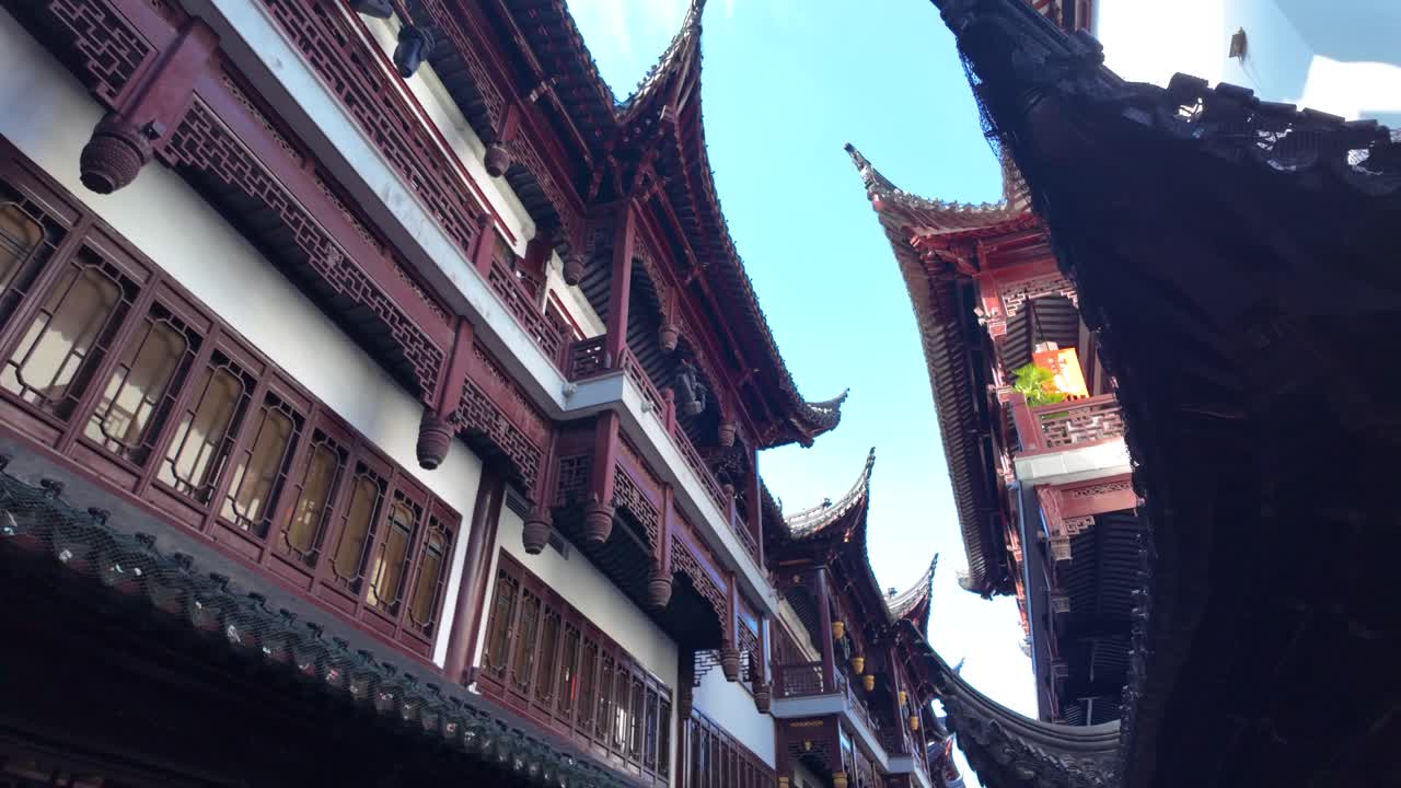 Slow motion upward view of ornate curved Chinese roofs with upturned eaves near Yu Garden Shanghai, blue sky background, daytime