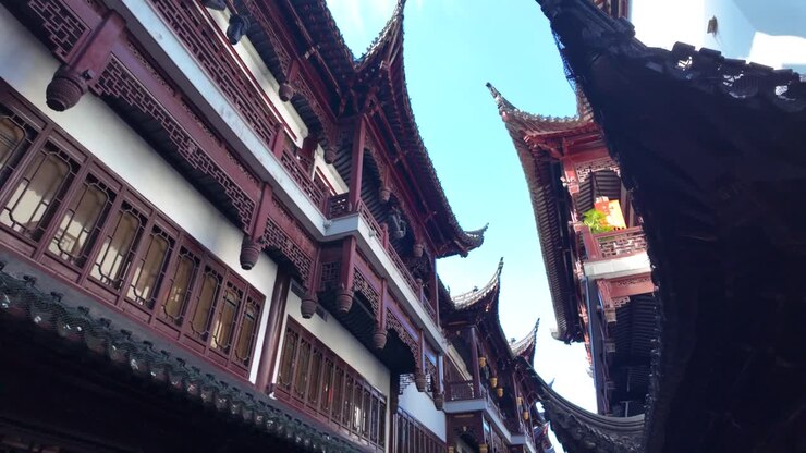 Vista em câmera lenta para cima de telhados chineses curvos e ornamentados com beirais virados para cima perto do Jardim Yu em Xangai, céu azul ao fundo, durante o dia