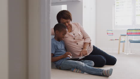 Abuela-Sentada-Con-Su-Nieto-En-El-Dormitorio-De-Los-Niños-Usando-Una-Tableta-Digital-Juntos